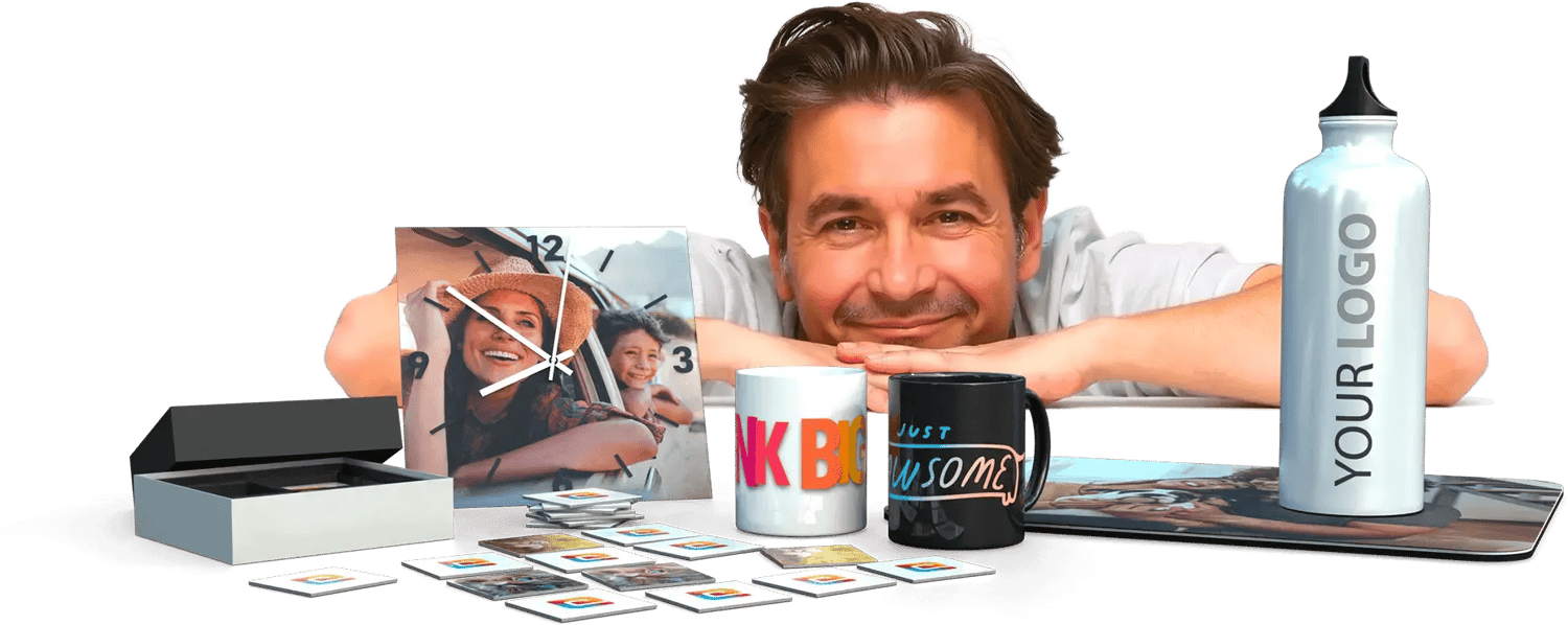 a smiling man resting his head and arms on a table full of customized products